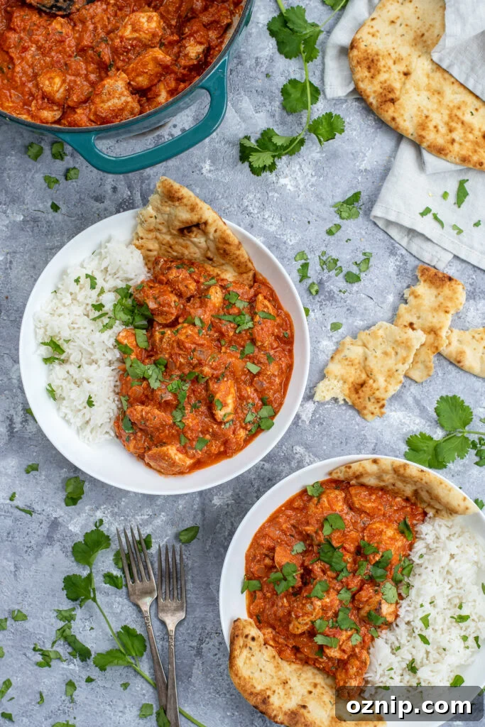 Flatly of two bowls and a dutch oven full of bright chicken tikka masala, covered with sprinkles of cilantro and pieces of naan bread.