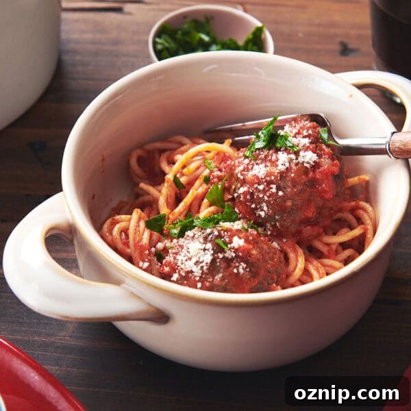 Spaghetti and meatballs with tomato sauce in white bowl on table.