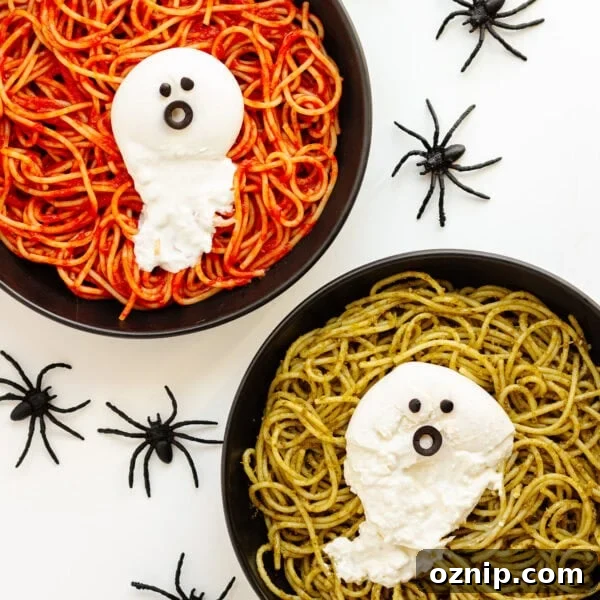Two plates of spaghetti (one with tomato sauce and one with pesto) topped with burrata ghosts and surrounded by spiders.