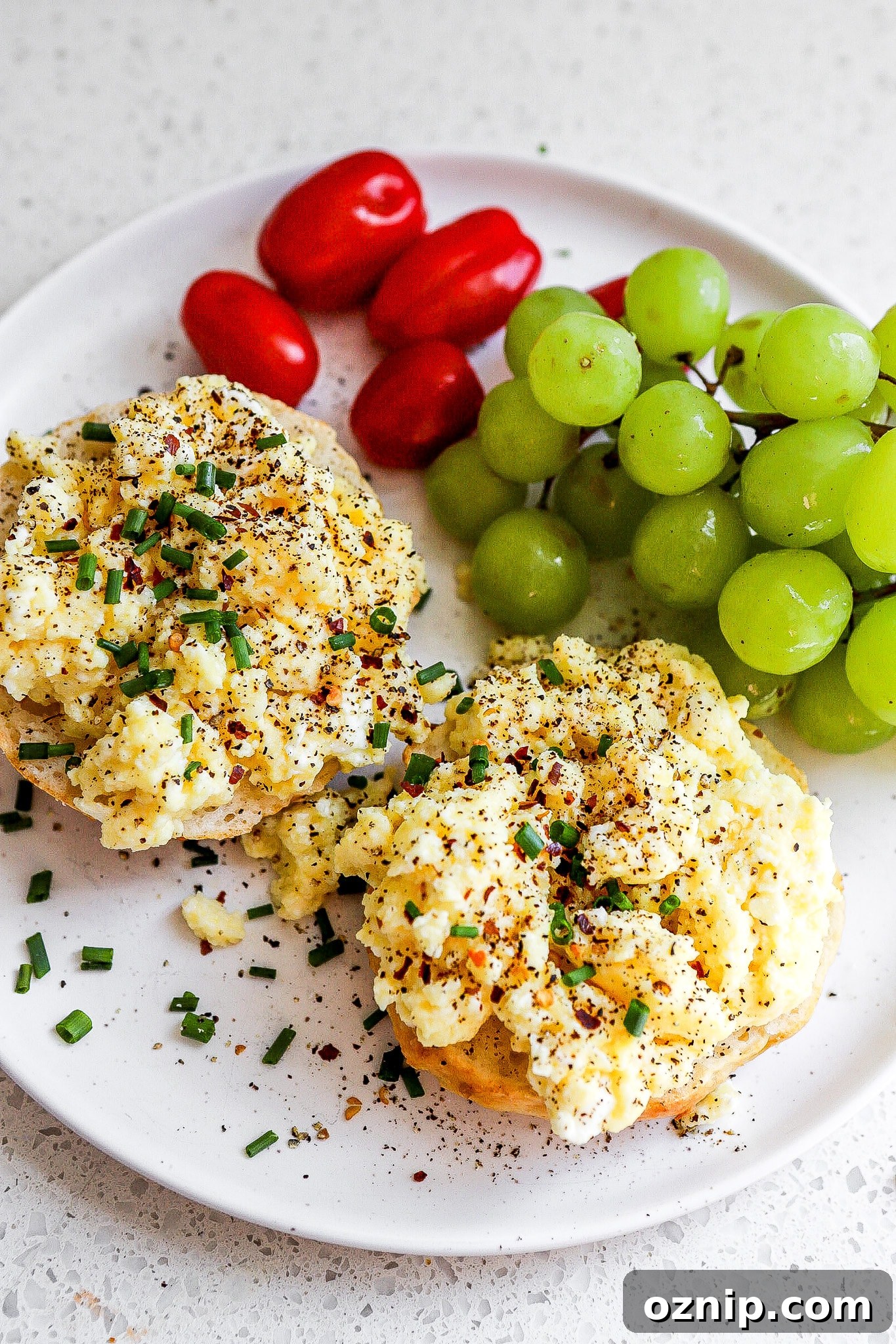 Top down view of cottage cheese eggs on a bagel with green grapes and cherry tomatoes.