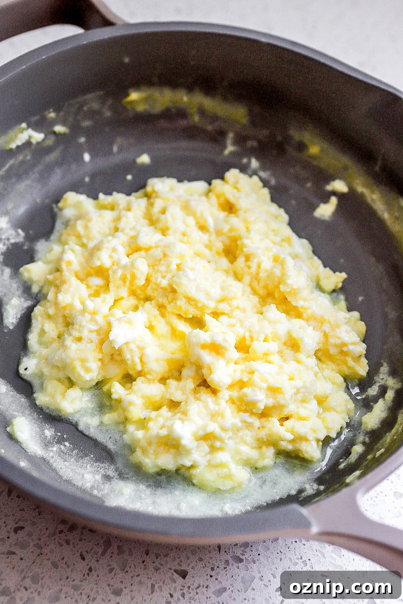 Side view of scrambled eggs with cottage cheese in small frying pan.