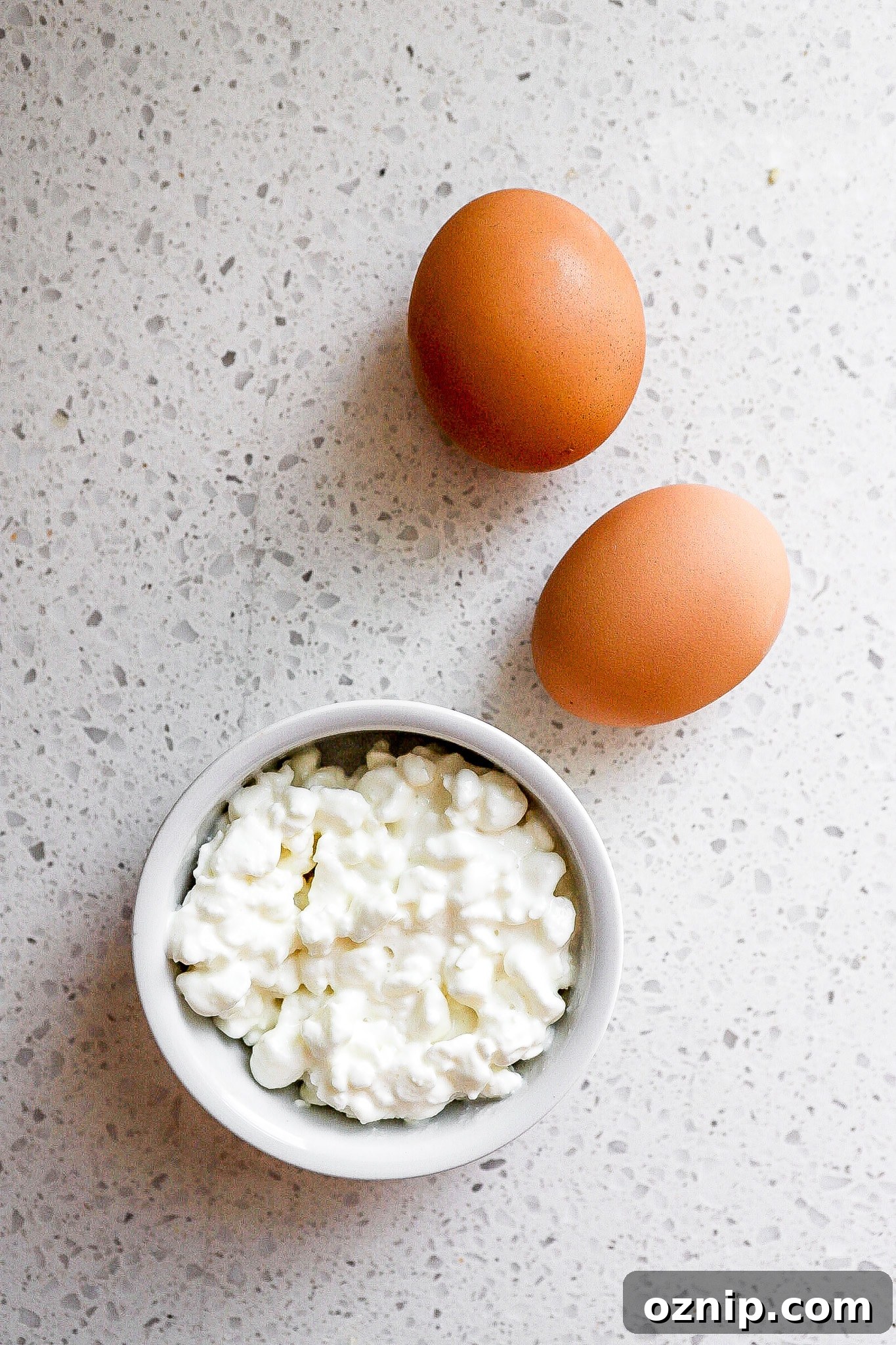 Top down view of 1/2 cup cottage cheese in small ramekin and 2 whole eggs.