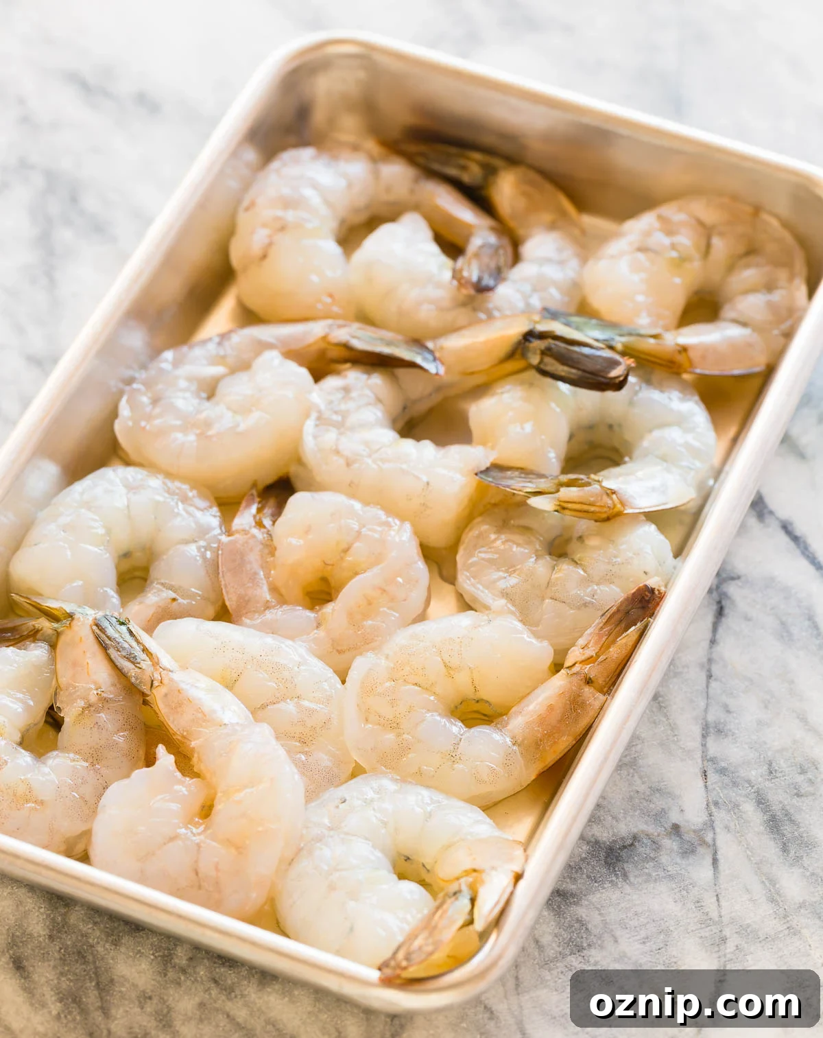 Raw shrimp peeled and cleaned on a rimmed baking sheet.