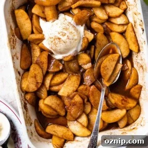 Baking dish filled with baked apples swimming in a cinnamon spiced syrup and topped with vanilla ice cream.