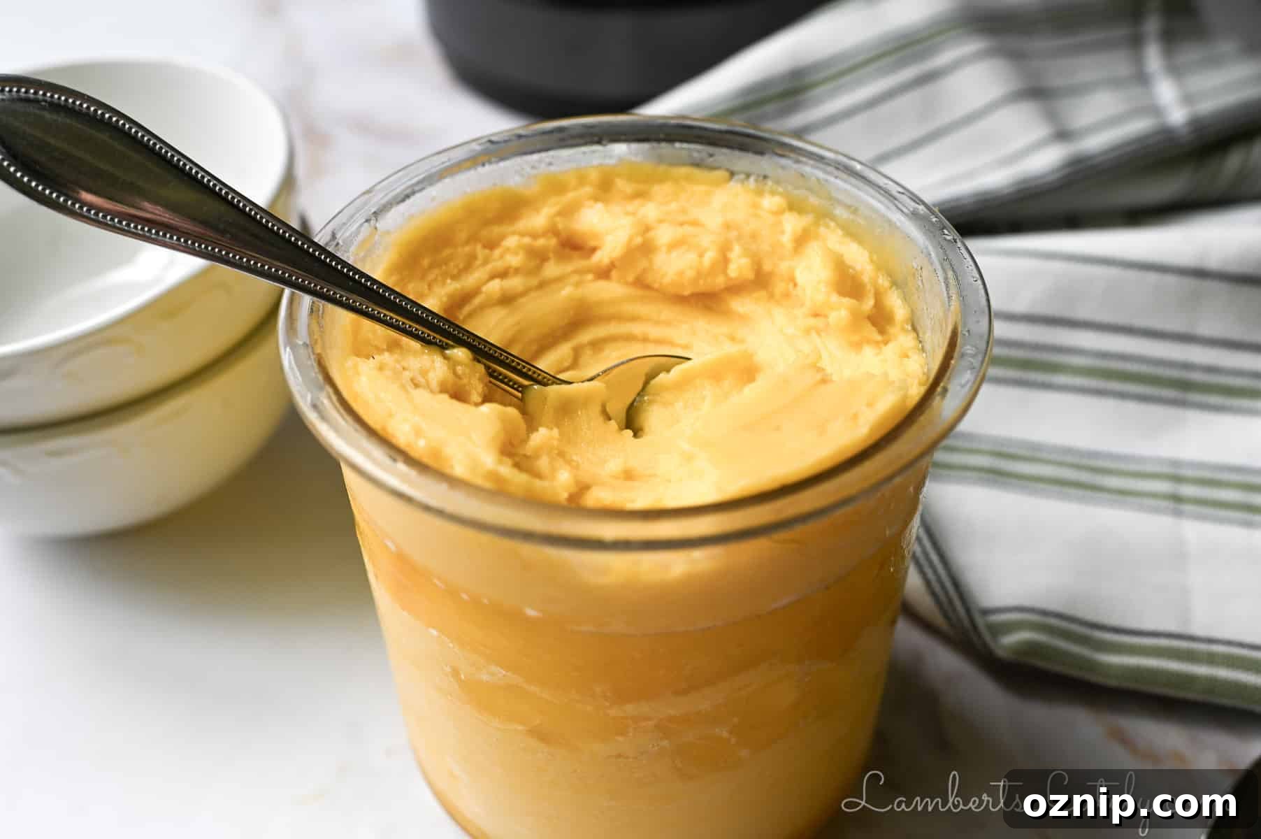 2 Ingredient Ninja Creami Mango Sorbet Recipe 2 pint container of ninja creami mango sorbet with a spoon in it, napkin, stack of bowls.