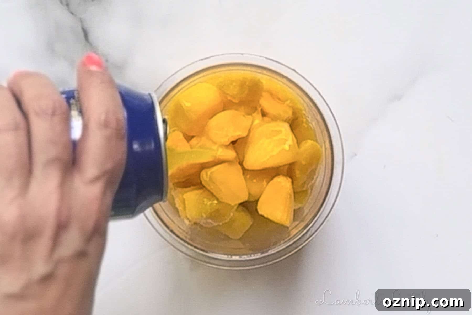 2 Ingredient Ninja Creami Mango Sorbet Recipe 6 Pouring canned mango nectar into a plastic Ninja Creami pint over frozen fruit pieces.