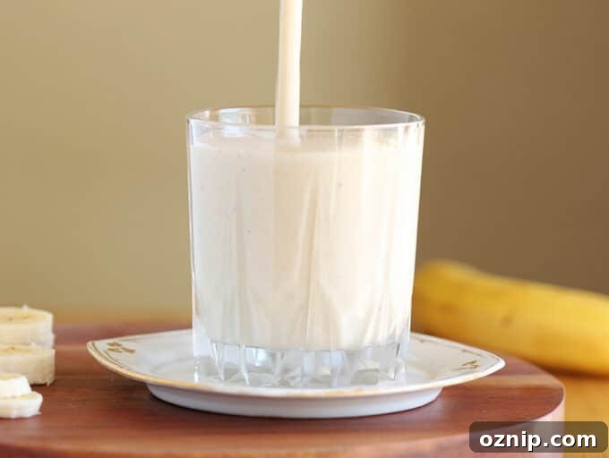 Smoothie being poured into a glass on a white plate.