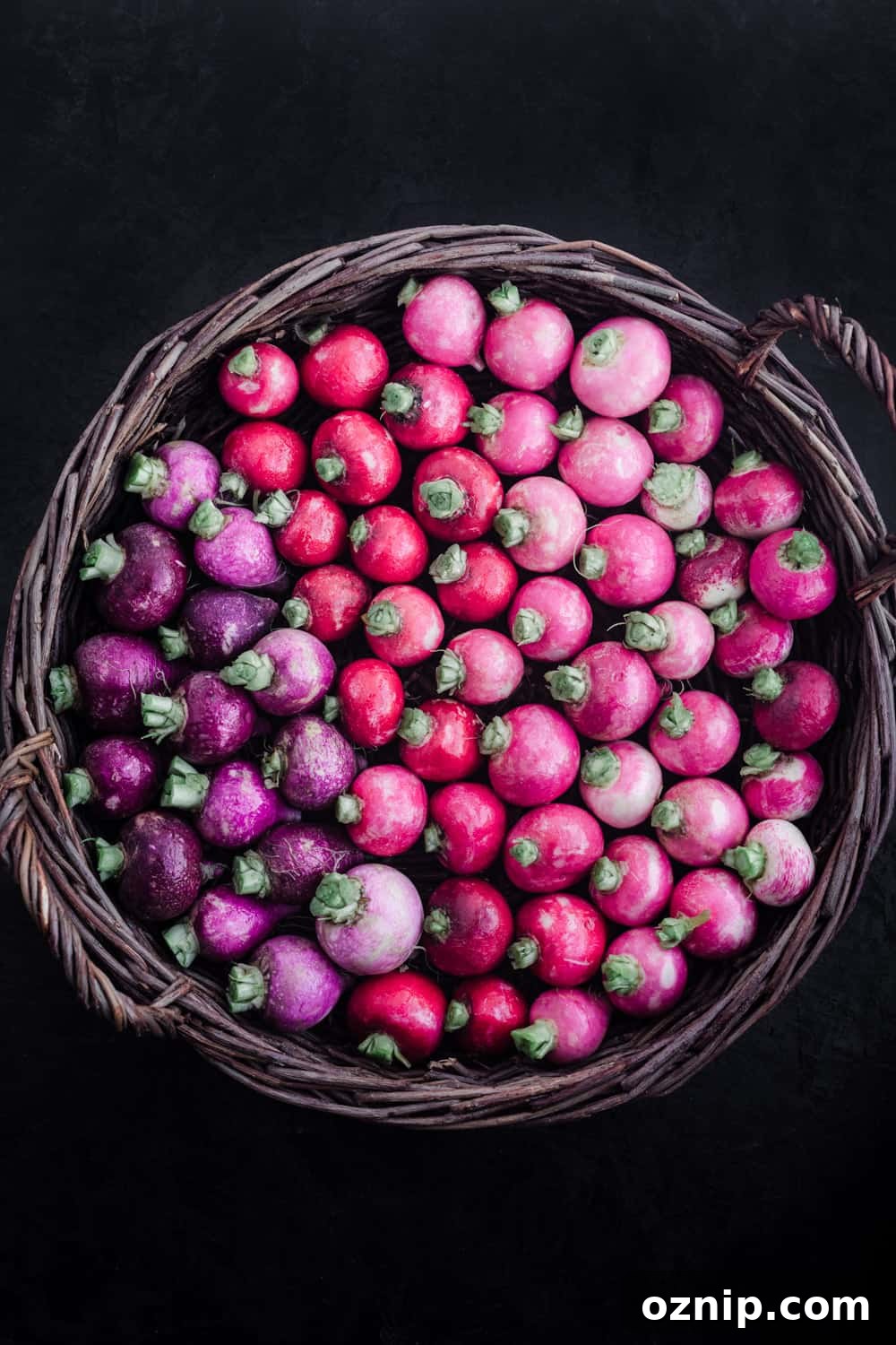 Basket filled with pink and purple radish varieties, overhead view on a dark background.