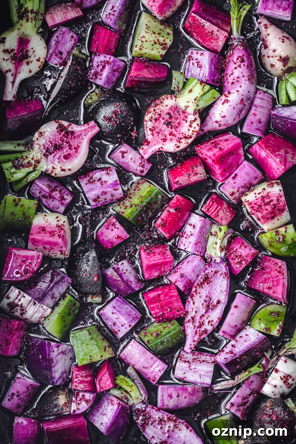 Mixed radish varieties tossed with olive oil and sumac before roasting, overhead view.