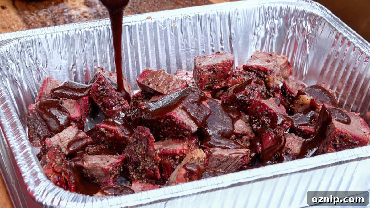 Ultra Tender Burnt Ends from Chuck Roast 8 Barbecue sauce being poured over smoked chuck roast in aluminum pan