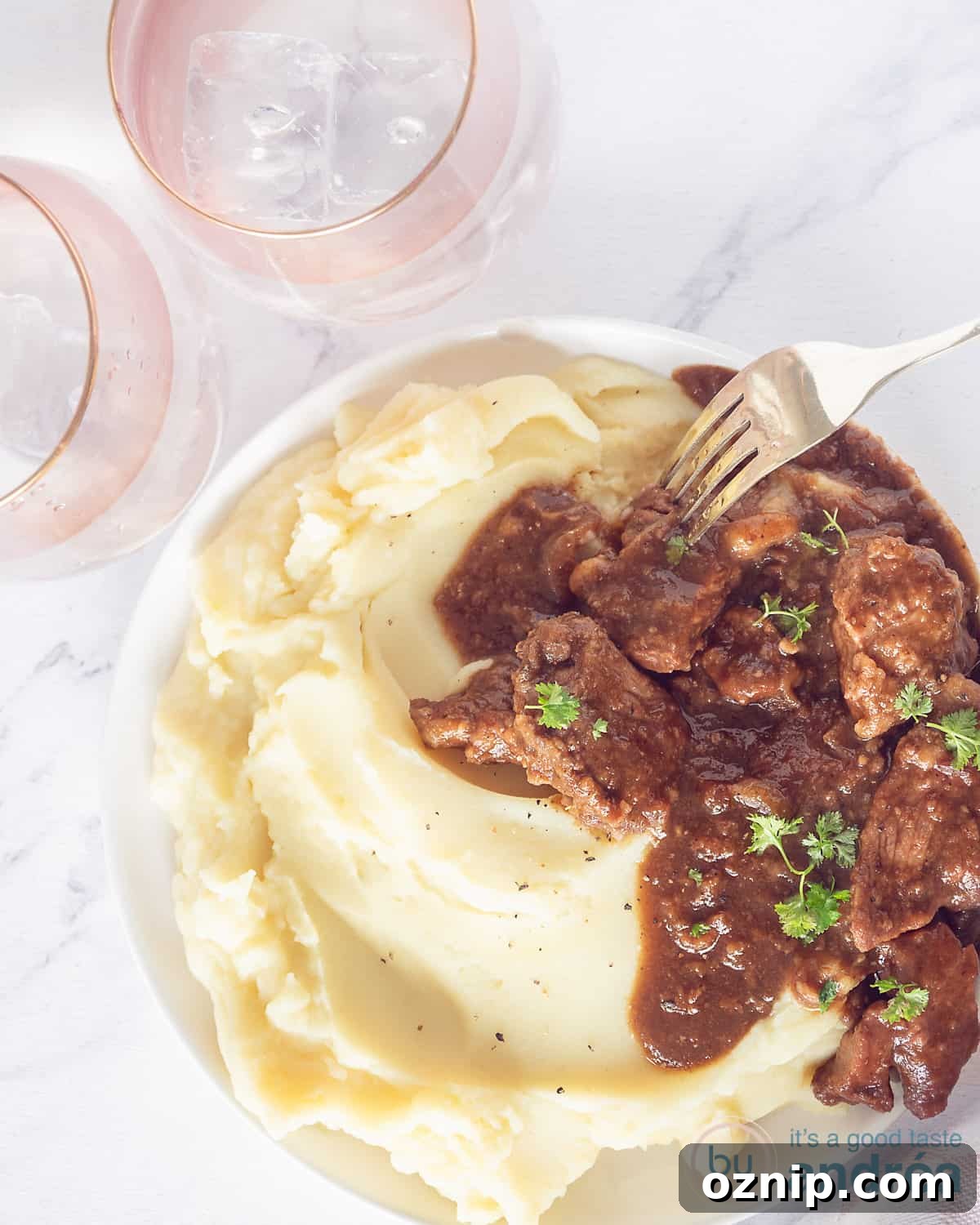Slow-Cooked Beef Stew with Apple Butter and Speculoos 2 top photo of a white plate with mashed potatoes and slow-cooked beef stew. A white background with two pink glasses