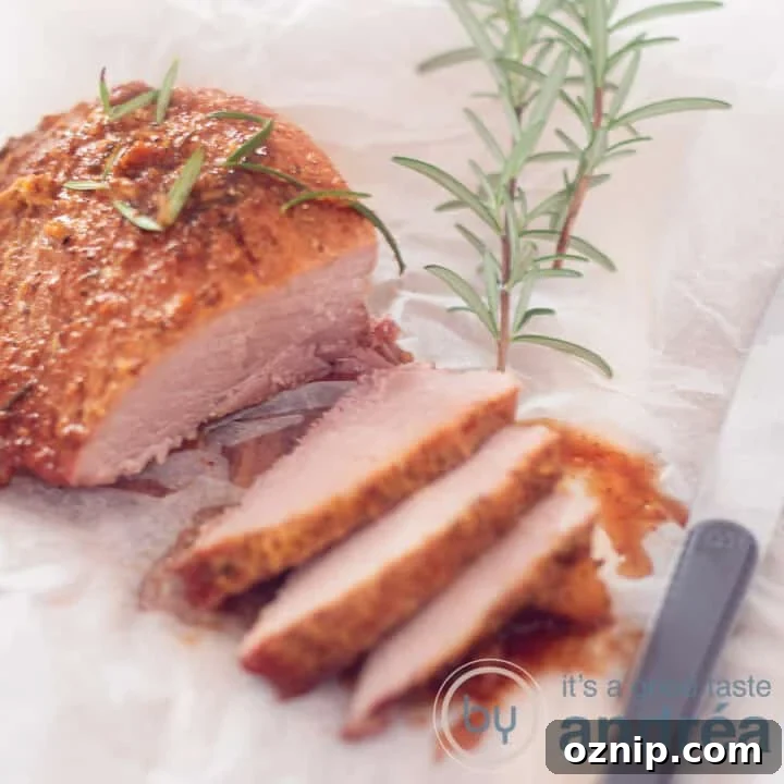 A square photo with a ham cut with three slices and gravy in front. A baking paper underneath and rosemary on top.