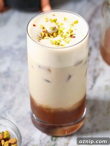 Iced pistachio latte in a tall glass sitting on a marble surface.
