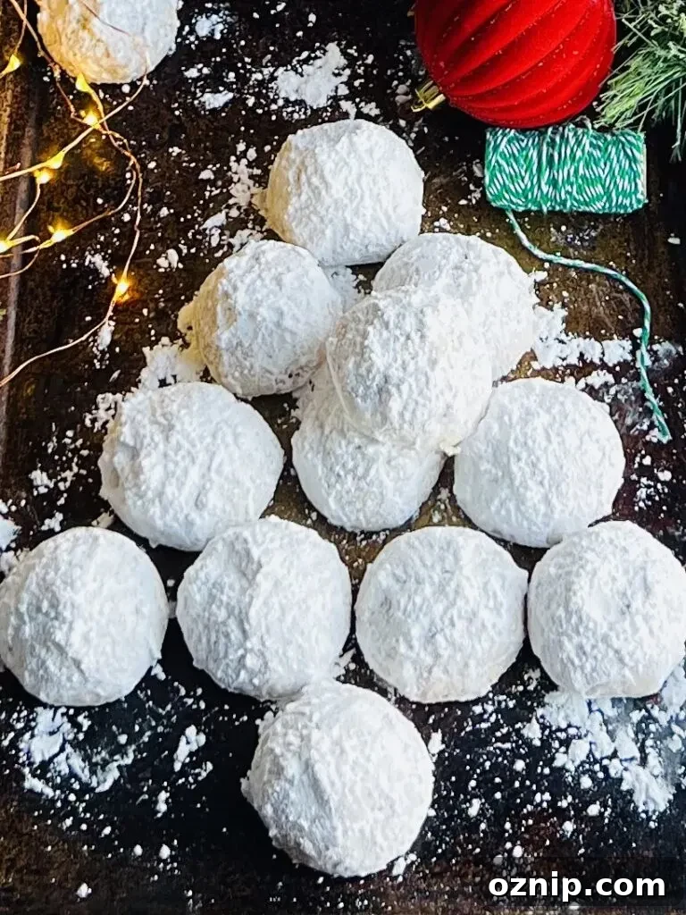 Pecan Snowball Cookies Recipe: Melt-in-Your-Mouth Holiday Treat 5 A dark baking sheet with white round cookies styled in the shape of a Christmas tree.