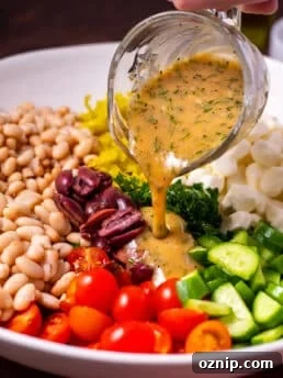 small glass pitcher of creamy herb dressing being poured over kale and cannellini bean salad