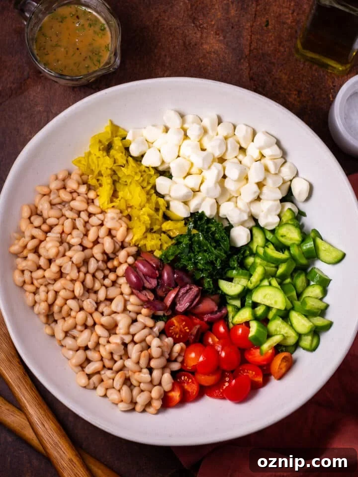 remaining salad ingredients added to the bowl: white beans, pepperoncinis, mozzarella pearls, olives, tomatoes and cucumbers