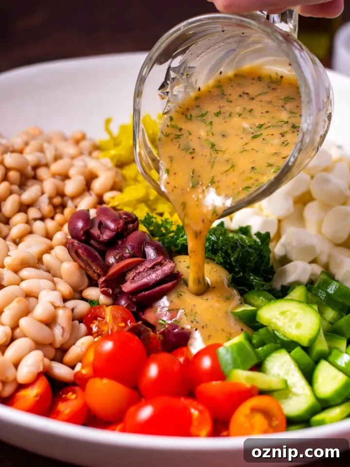 small crystal pitcher pouring dill mustard dressing on kale and cannellini bean salad