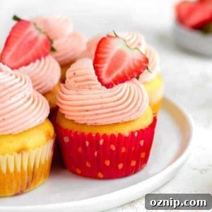 Side view of easy strawberry cupcakes on a white plate, topped with halved fresh strawberries