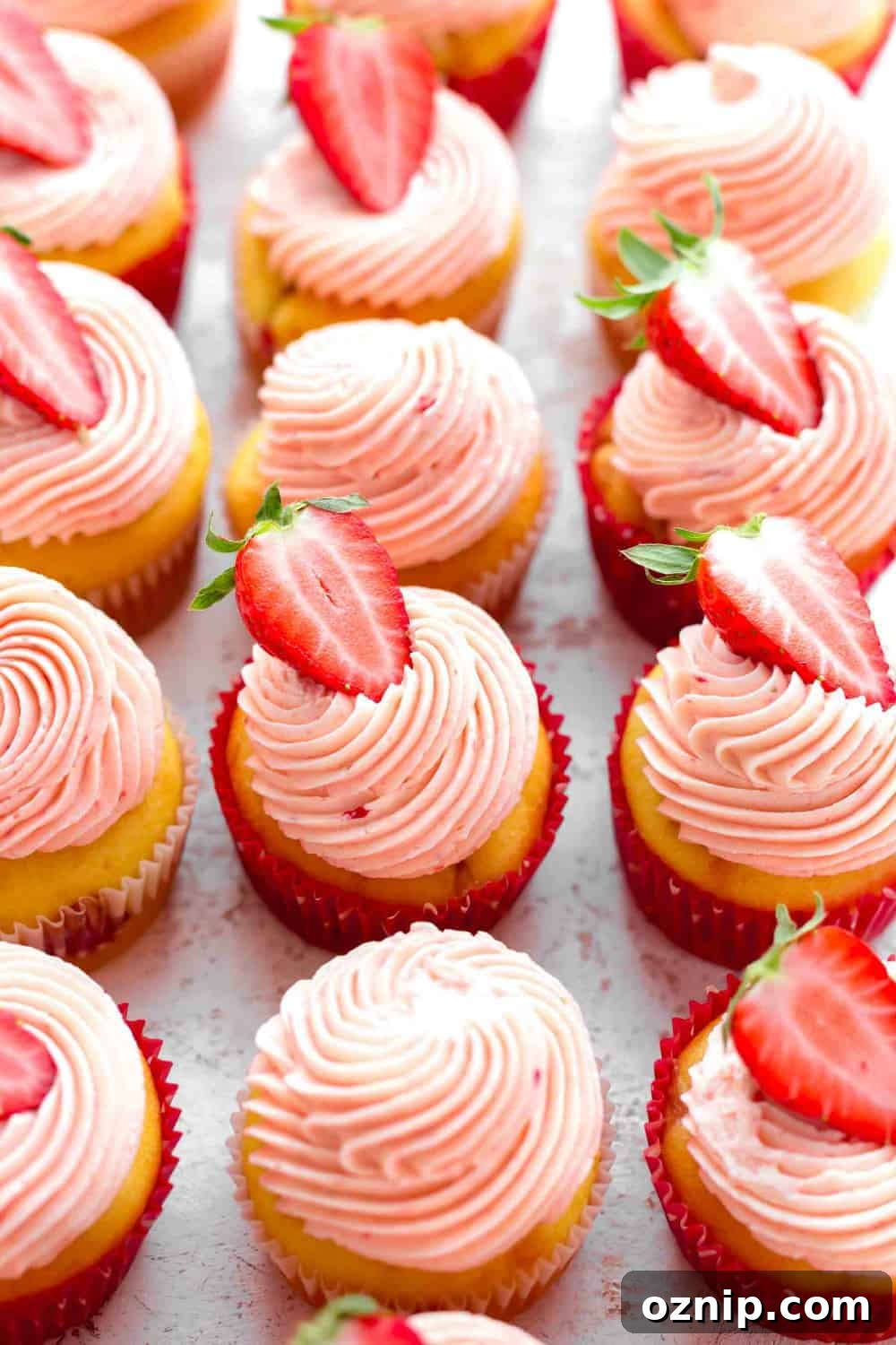 45-degree view of cupcakes topped with strawberry buttercream and halved strawberries on white surface