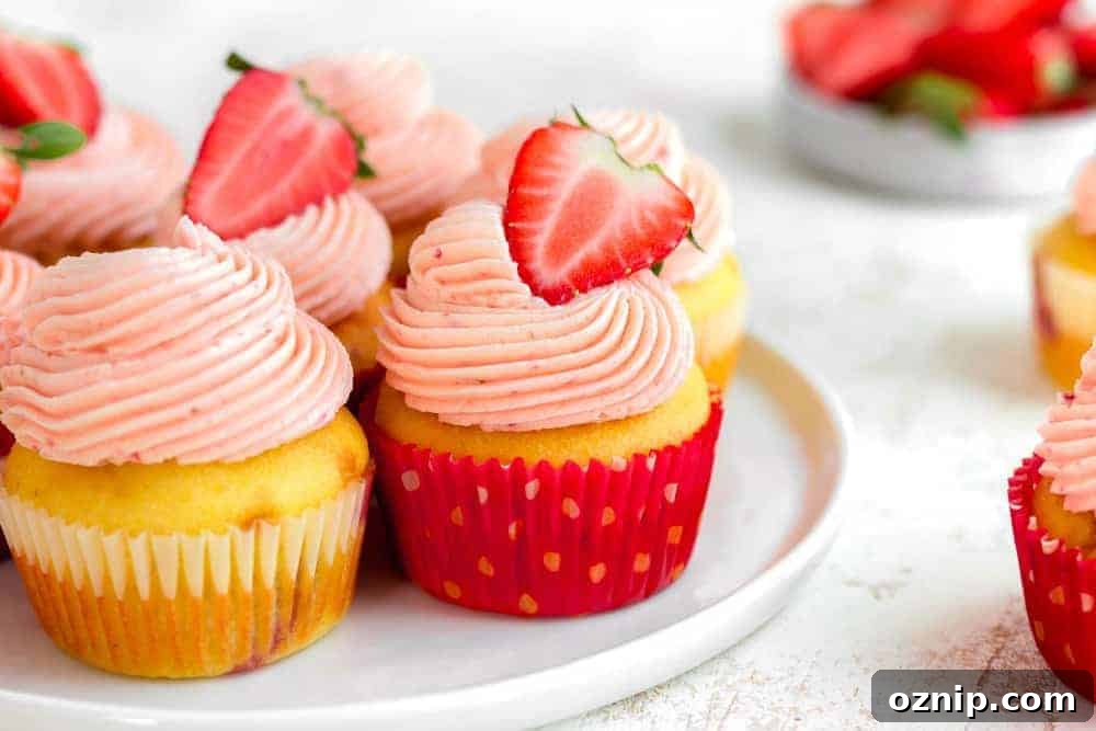 Side view of easy strawberry cupcakes on a white plate, topped with halved fresh strawberries