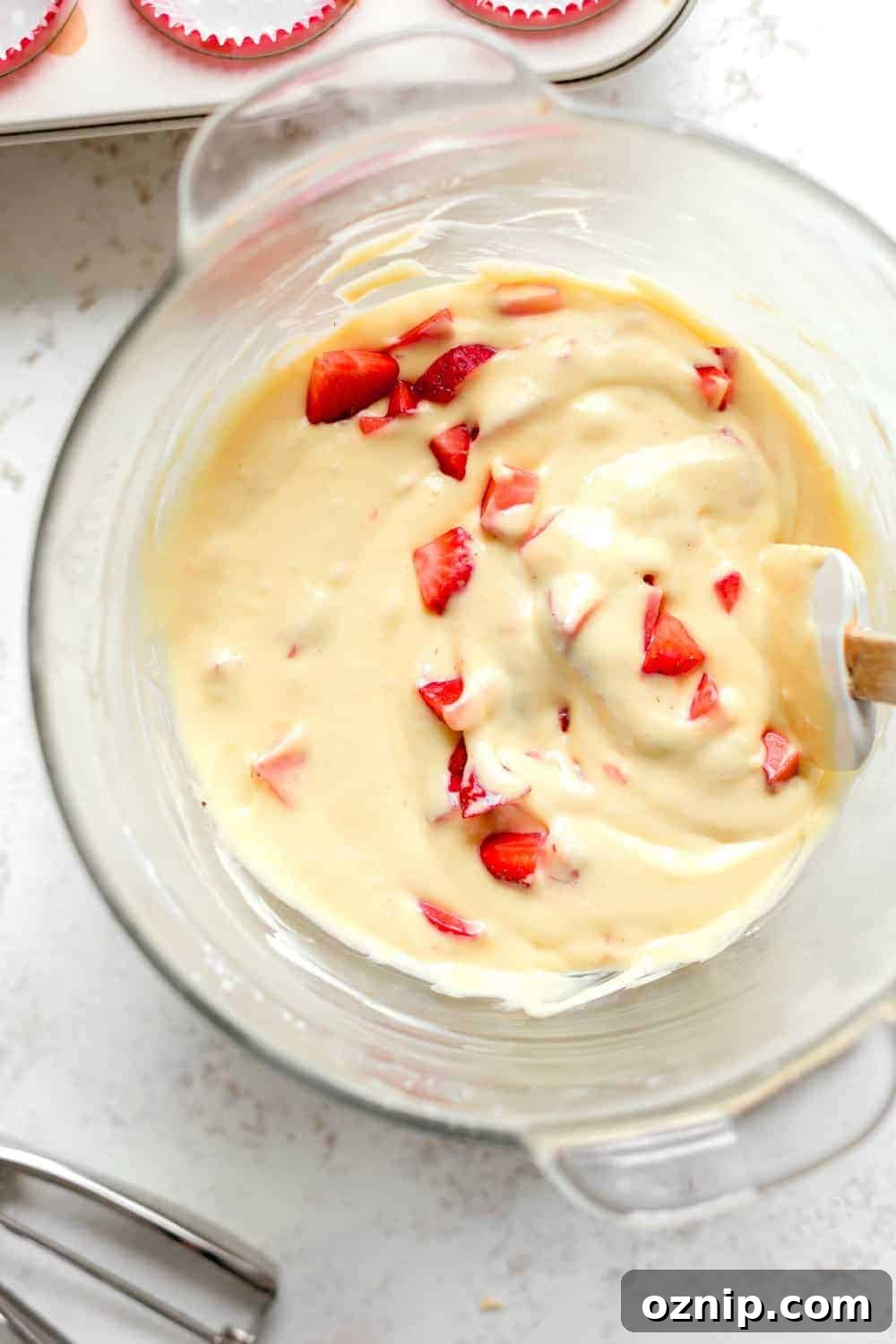 Overhead view of diced strawberries mixed into cupcake batter in glass bowl