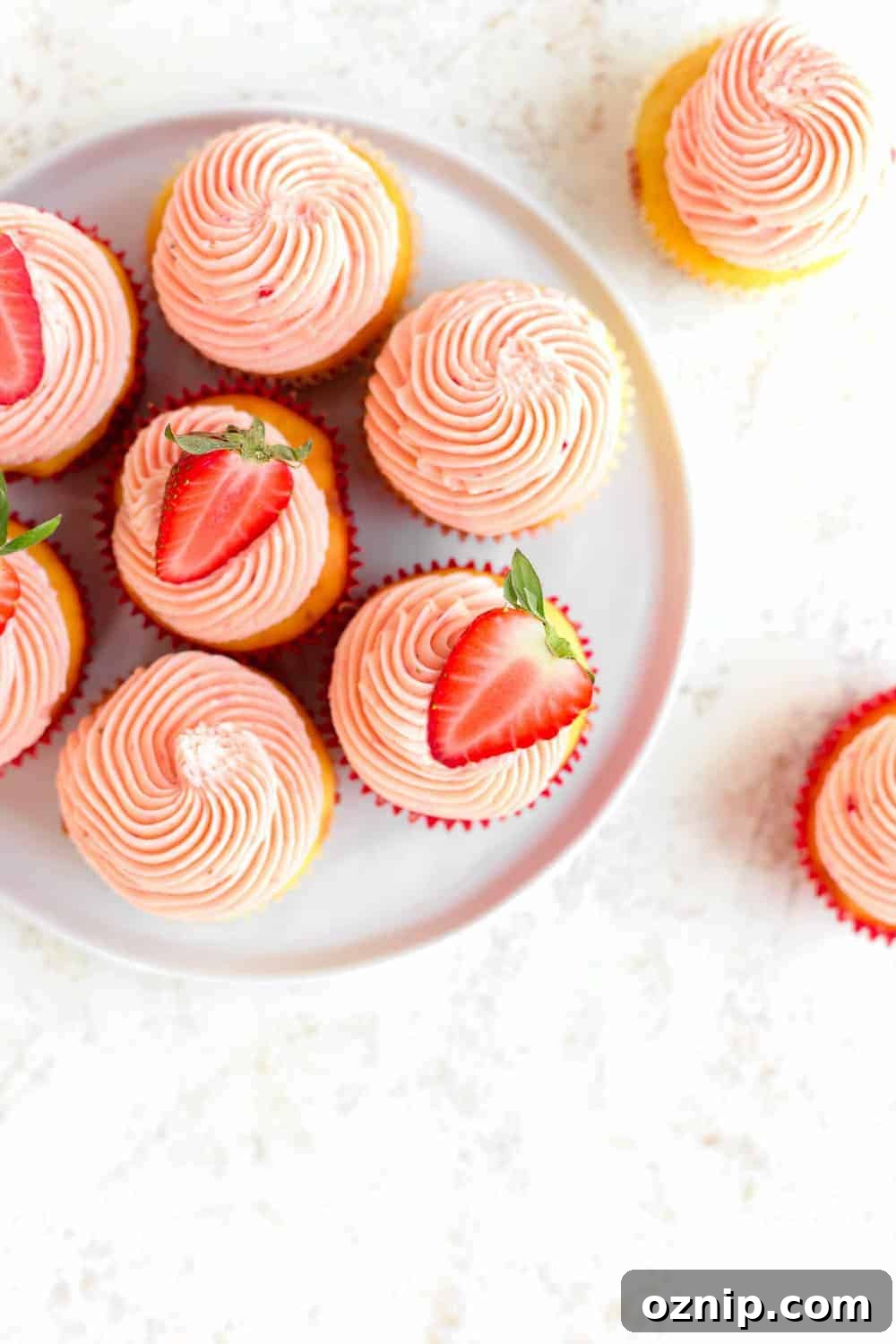 Overhead shot of easy strawberry cupcakes on a white plate, topped with halved strawberries