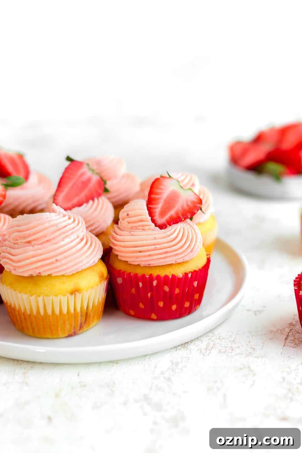 Side view of easy strawberry cupcakes topped with strawberry buttercream on a white plate