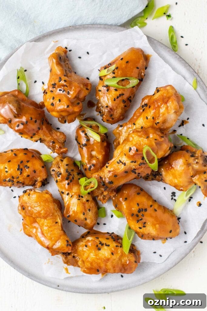 Chicken wings shown tossed in a thick Asian sauce garnished with black sesame seeds and green onions.