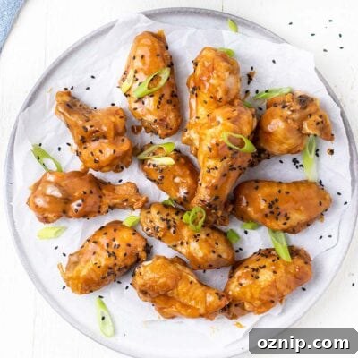Chicken wings shown tossed in a thick Asian sauce garnished with black sesame seeds and green onions.