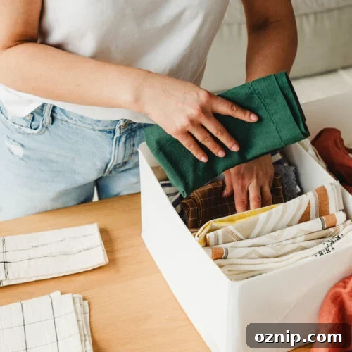 Closeup of a woman folding towels and placing them neatly into a storage bin, illustrating simple home organizing tips.