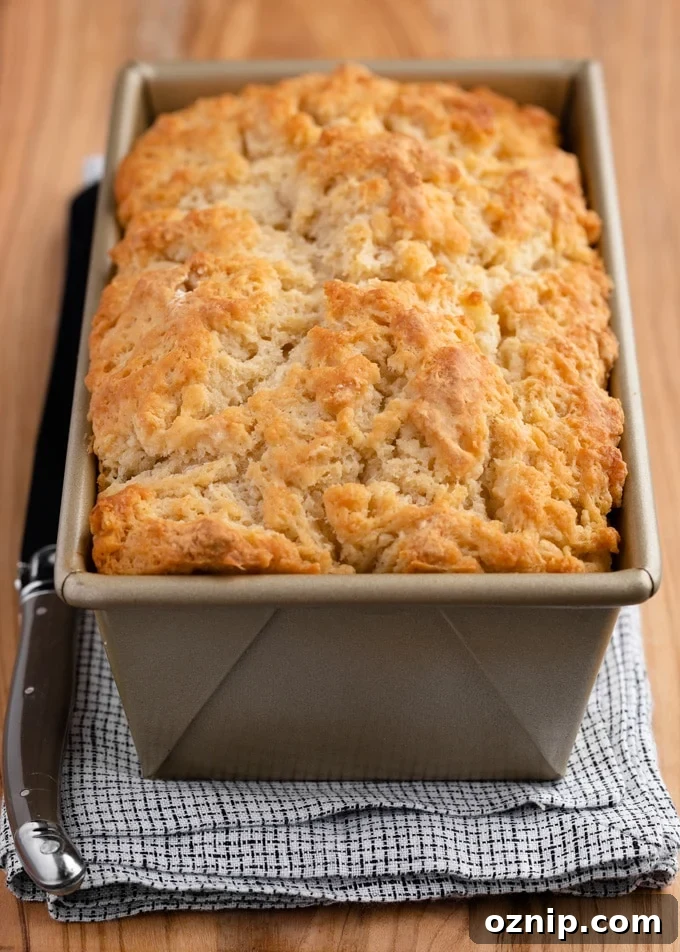 Classic Beer Bread Recipe with Crispy Crust 5 baked loaf of beer bread in a gold loaf pan on a wooden board with a white and blue checked napkin