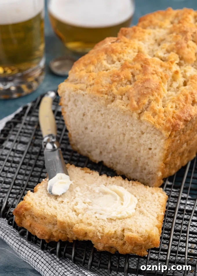Classic Beer Bread Recipe with Crispy Crust 6 a slice of beer bread next to the baked loaf on a black cooling rack, spread with softened butter