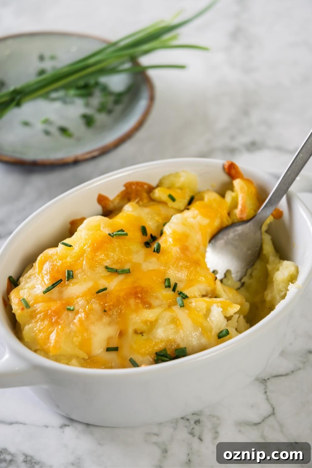 A spoon in a casserole dish with cheesy mashed potatoes.