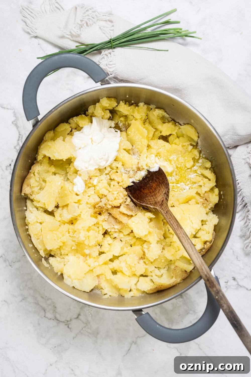 Mashed potatoes and sour cream in a pot with a wooden spoon.