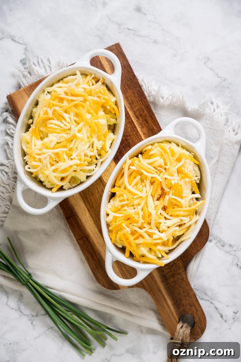 Two casserole dishes filled with shredded cheddar cheese with mashed potatoes beneath it.