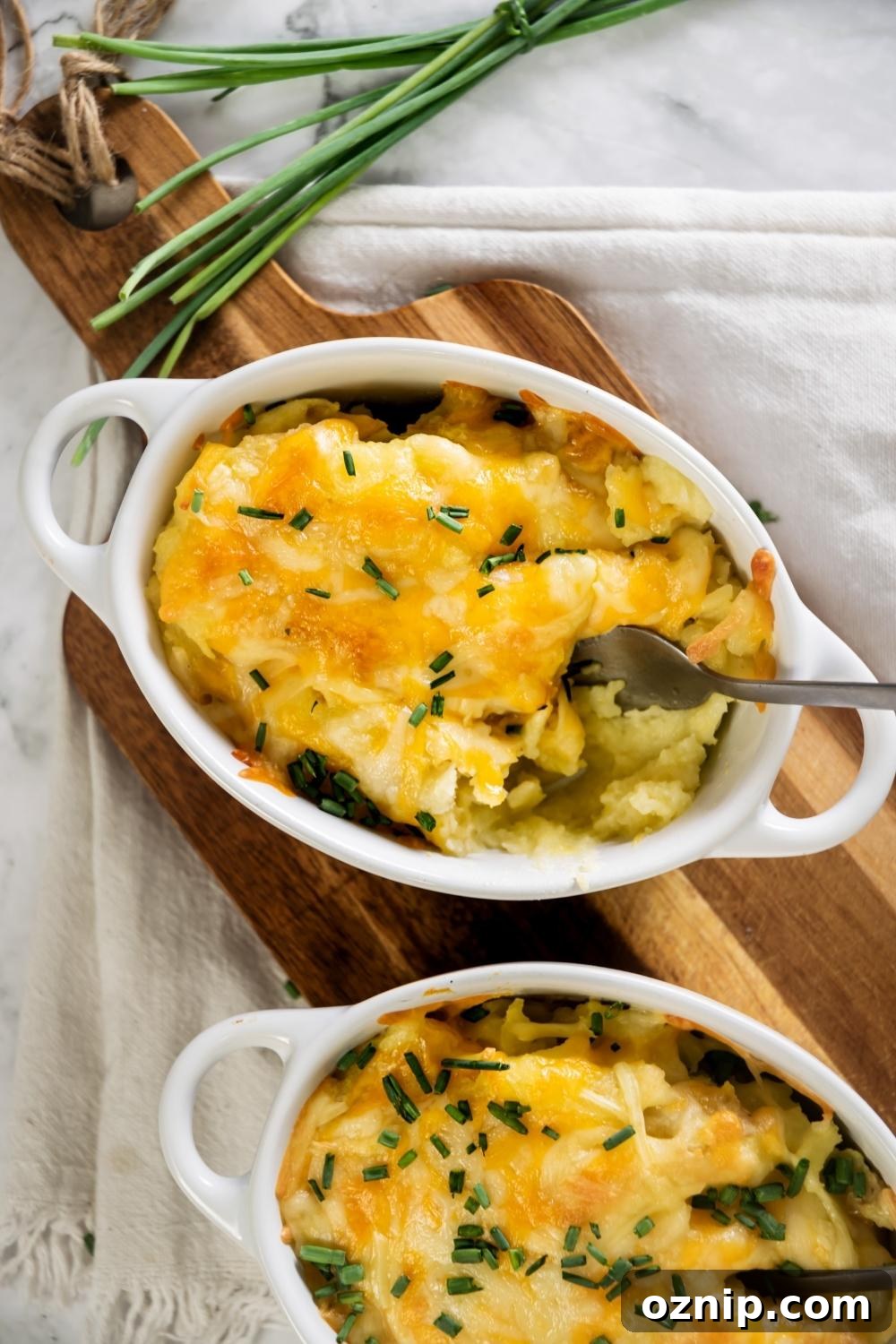 Cheesy mashed potatoes in a white casserole dish on a wooden cutting board.