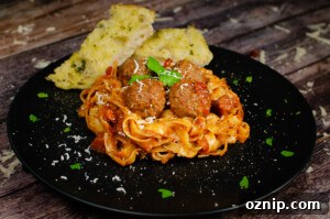 Spicy Meatball Pasta served on a black plate with garlic bread on the side with a garnish of chopped parsley and grated parmesan over the top of the food