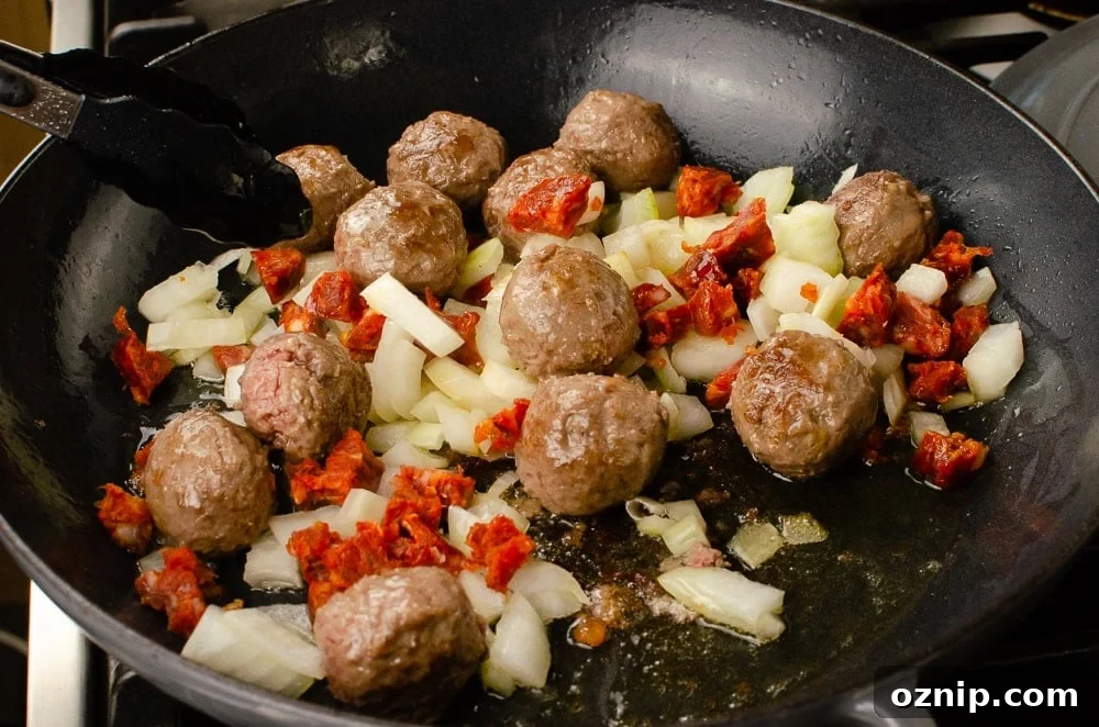 Meatballs, chopped onions and chopped chorizo cooking in olive oil in a grey cast iron pan