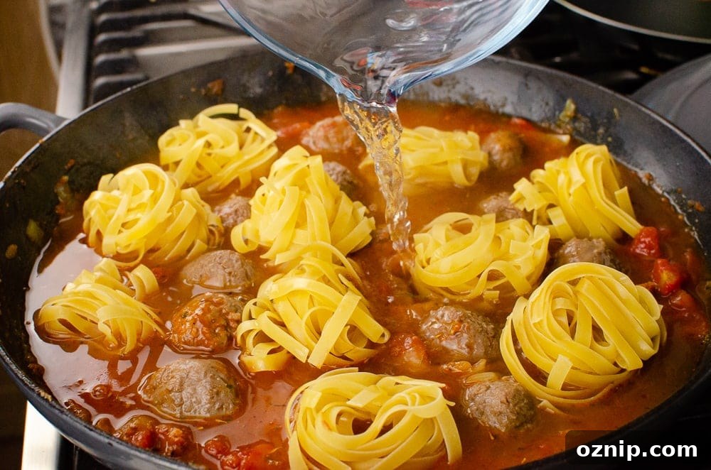 Balls of tagliatelle placed into the cast iron dish and pouring water in with the meat balls from a glass jug