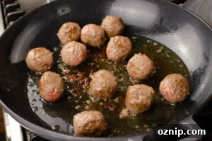 Beef meatballs cooking in olive oil in a grey cast iron pan