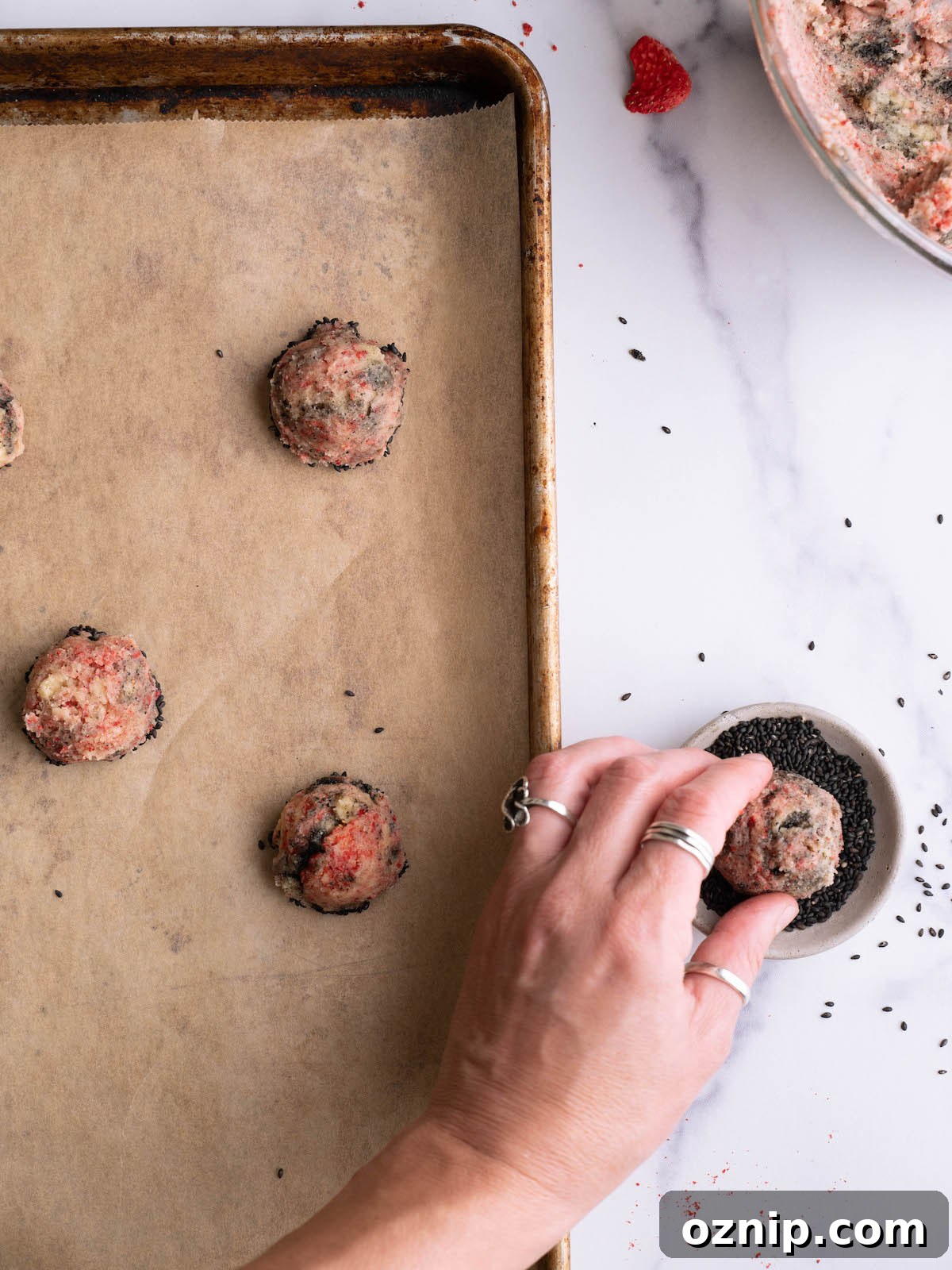 Dipping strawberry swirl cookies into black sesame seeds