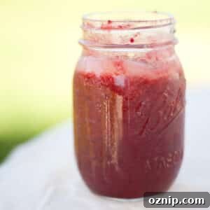 a mason jar of cherry plum jam on a white table cloth in front of a green lawn.