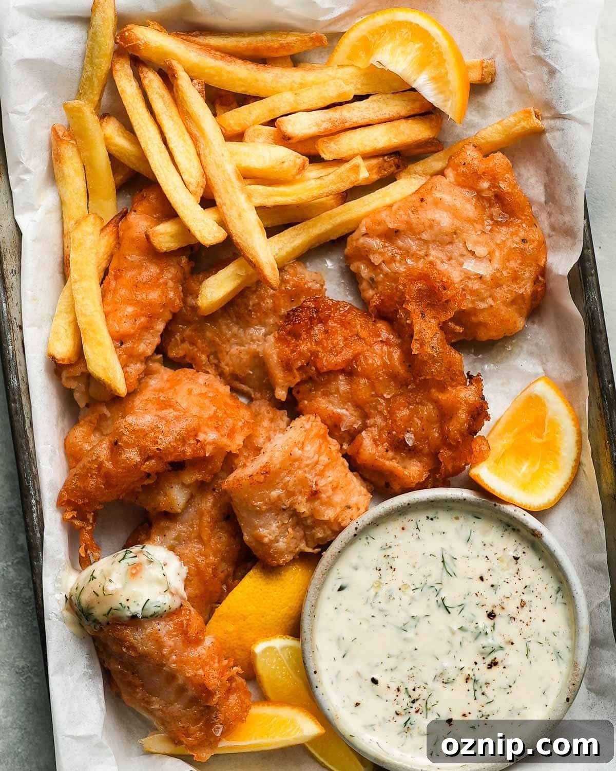 Fried cod with fries, lemon wedges, and tartar sauce on a tray.