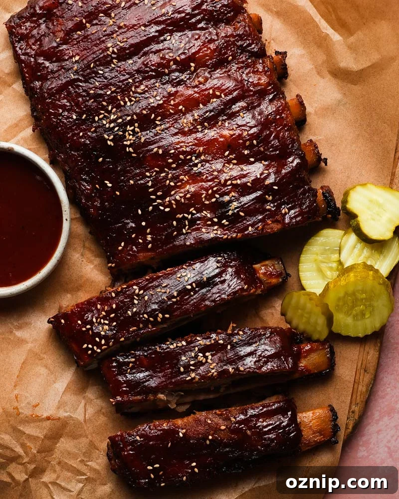 Barbecue ribs with sesame seeds, sauce, and pickles on brown parchment paper.