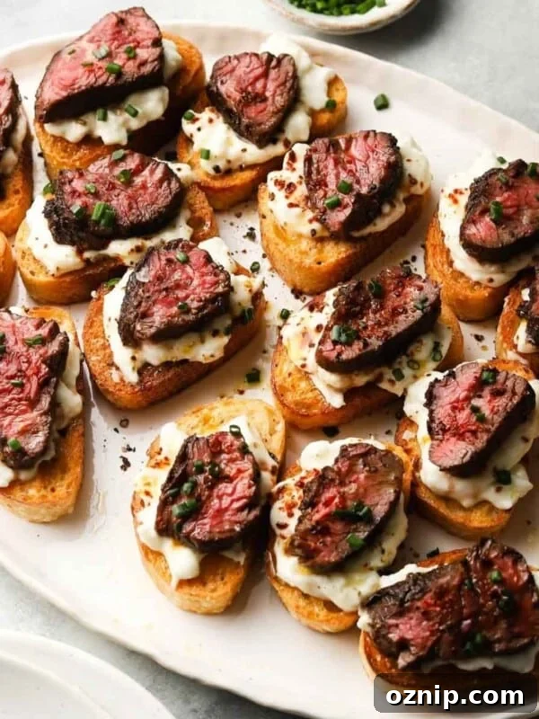 Crostini topped with creamy burrata, seared steak, and fresh herbs on a white platter.