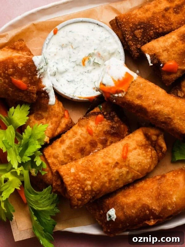 Crispy buffalo chicken egg rolls with dipping sauce and celery garnish on a platter.