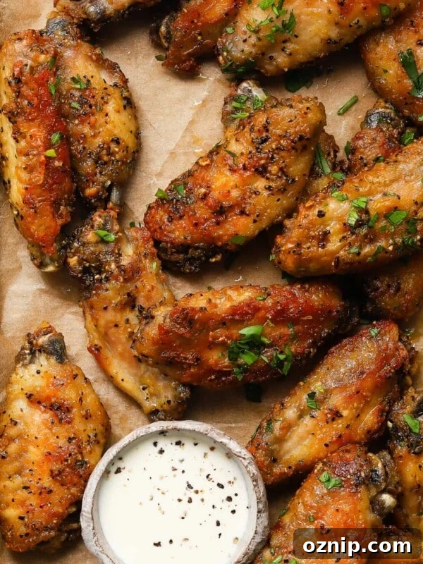Crispy lemon pepper wings on parchment with dipping sauce garnished with herbs.