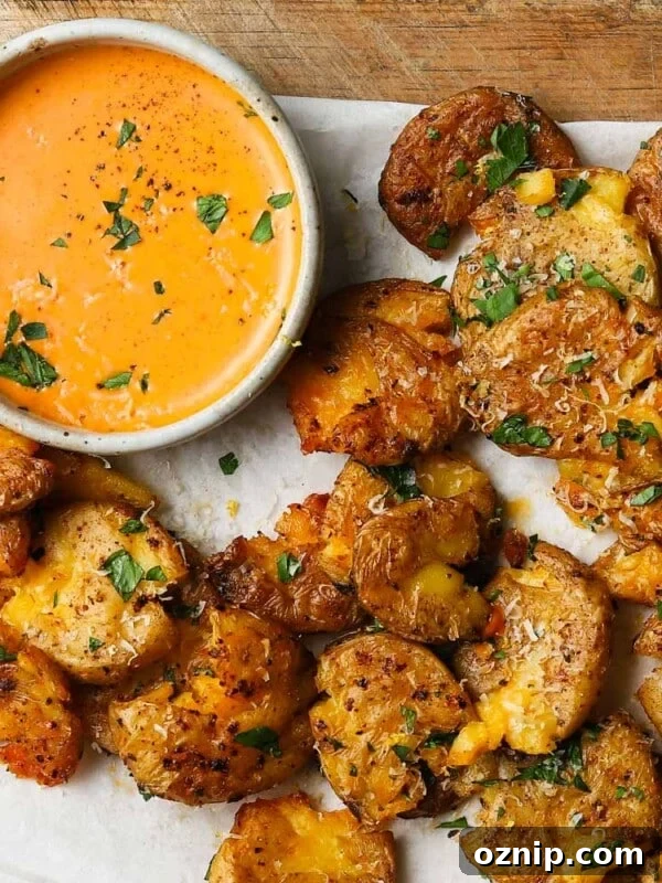 Crispy smashed potatoes with herbs beside a bowl of spicy orange mayo dip.