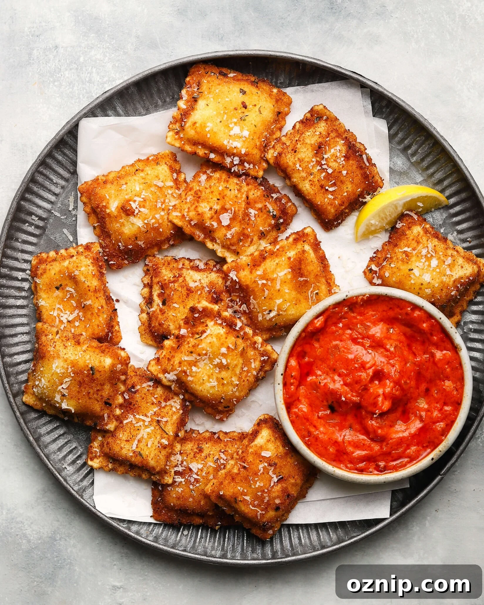Golden toasted ravioli with tomato sauce and lemon wedge on a plate.