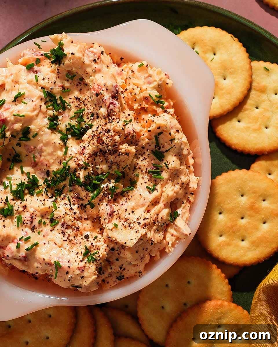 Cheddar pimento cheese dip garnished with chives, surrounded by round crackers.